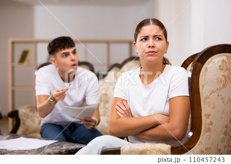Portrait of frustrated sad woman in living room, while disgruntled husband scolds her 110457243