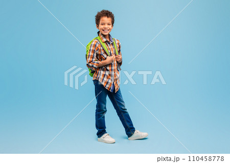 Smiling boy with backpack in plaid shirt, blue background 110458778