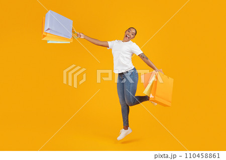 Happy black buyer woman jumps holding paper shopping bags, studio Happy black buyer woman jumps holding paper shopping bags, studio 110458861