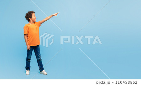 Excited boy pointing in the air at free space on blue backdrop 110458862