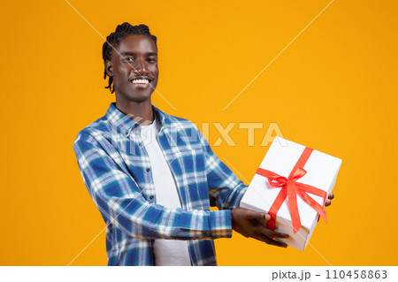 Happy young black man extending white gift box with red ribbon 110458863