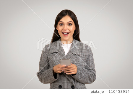 Surprised businesswoman holding smartphone, excited, looking at camera Surprised businesswoman holding smartphone, excited, looking at camera 110458914