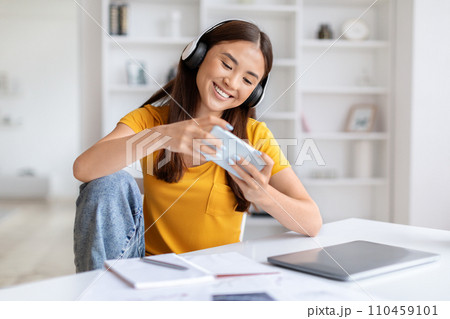Cheerful Asian Woman In Headphones Playing Video Games On Smartphone At Home 110459101