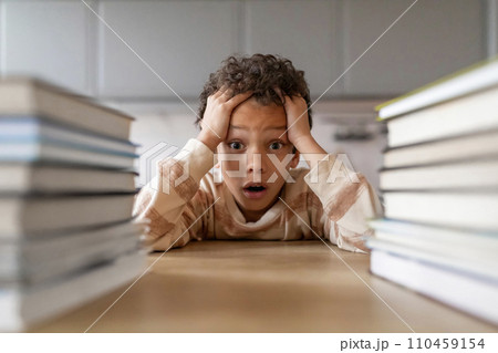 Stressed black boy surrounded by towering stacks of books 110459154