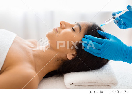 Beautician making scalp injections for smiling young indian lady Beautician making scalp injections for smiling young indian lady 110459179