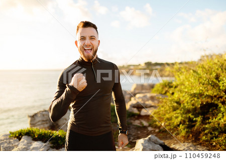 Ecstatic man celebrating with fist pump by the ocean 110459248