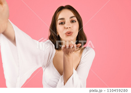 Charming young woman taking a selfie, blowing a kiss towards the camera 110459280