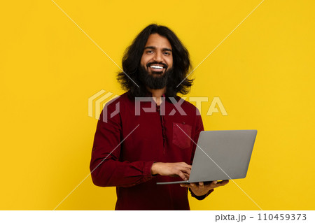 Cheerful young indian guy student using laptop Cheerful young indian guy student using laptop 110459373