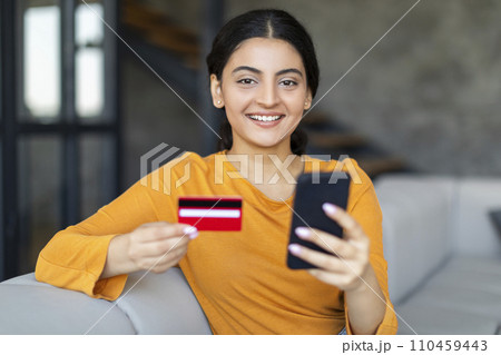 Cheerful Indian woman with credit card in hand making online payment 110459443