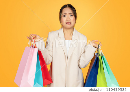Sad confused young chinese lady shopaholic with colorful bags, with purchases 110459523