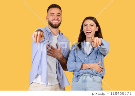 Laughing couple pointing at camera in casual clothes on yellow background 110459573