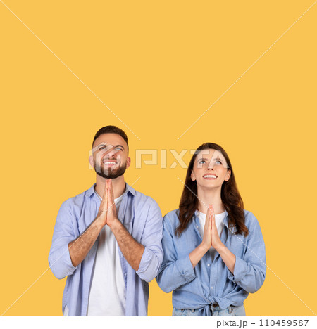Hopeful couple with hands in prayer position, looking up at copy space 110459587
