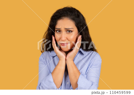 Worried young woman with curly hair holding her face in hands, looking 110459599