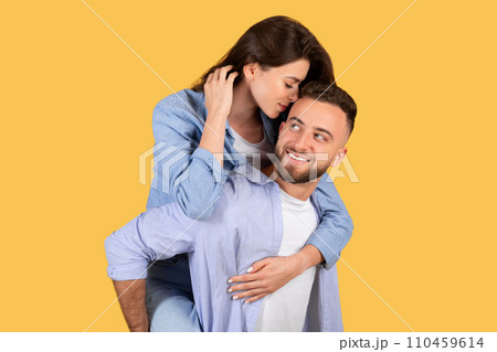 Woman whispers to man carrying her on yellow backdrop 110459614