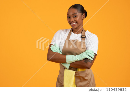 african american lady cleaner in apron posing crossing hands, studio 110459632