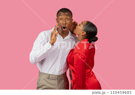 Black woman whispering to surprised man, both in elegant attire, pink background Black woman whispering to surprised man, both in elegant attire, pink background 110459685