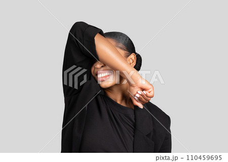 Joyful African American businesswoman playfully covering her eyes with one arm 110459695