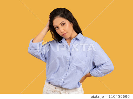 A confident young woman with dark hair wearing a casual blue shirt poses thoughtfully 110459696