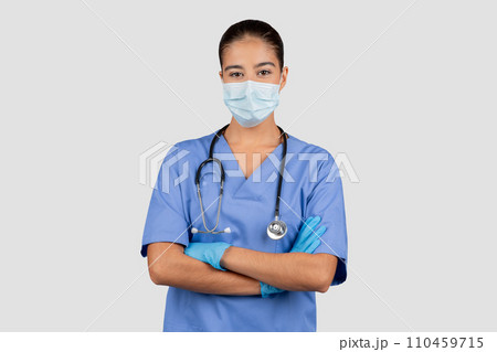 Glad caucasian millennial lady doctor or nurse in blue uniform, protective mask, gloves with crossed arms Glad caucasian millennial lady doctor or nurse in blue uniform, protective mask, gloves with crossed arms 110459715