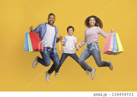 Seasonal Sales Concept. Happy Black Family Of Three Jumping With Shopping Bags 110459723
