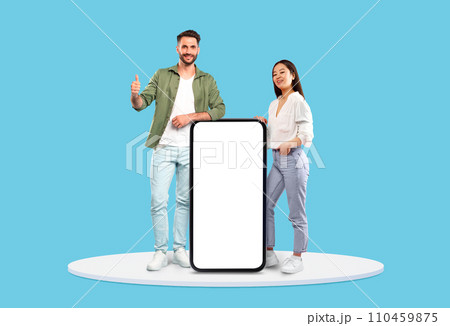 Diverse man and woman showcasing blank mobile screen, blue background 110459875