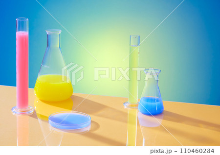 Test tubes, erlenmeyer flasks and petri dishes are used to store colored liquids on a blue-yellow gradient background. Simulation laboratory space. 110460284