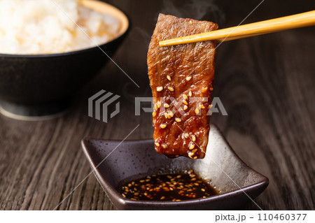 焼肉をタレをつけて食べる 110460377
