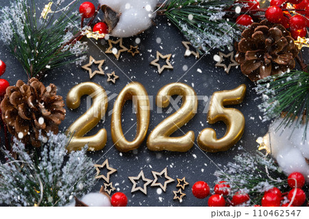 The golden figures 2025 made of candles on a black stone slate background are decorated with a festive decor of stars, sequins, fir branches, balls and garlands. Greeting card, happy New Year. The golden figures 2025 made of candles on a black stone slate background are decorated with a festive decor of stars, sequins, fir branches, balls and garlands. Greeting card, happy New Year. 110462547