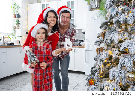 Happy family in santa hats with tiny house in cozy home with Christmas decor of festive white kitchen. Gift for New Year. Insurance, moving to new house, mortgage, rent and purchase real estate 110462720