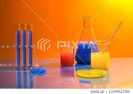 Advertising scene with laboratory equipments - test tubes, erlenmeyer flask, beakers and petri dish with colorful liquid inside decorated on orange gradient background. Space for design Advertising scene with laboratory equipments - test tubes, erlenmeyer flask, beakers and petri dish with colorful liquid inside decorated on orange gradient background. Space for design 110462760