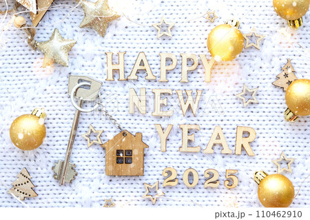 House key with keychain cottage on festive background with stars, lights of garlands. New Year 2025 wooden letters, greeting card. Purchase, construction, relocation, mortgage, insurance 110462910