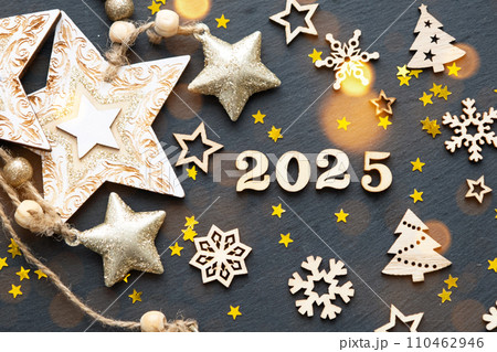 Happy New Year-wooden letters and the numbers 2025 on festive black background with sequins, stars, snow. Greetings, postcard. Calendar, cover 110462946