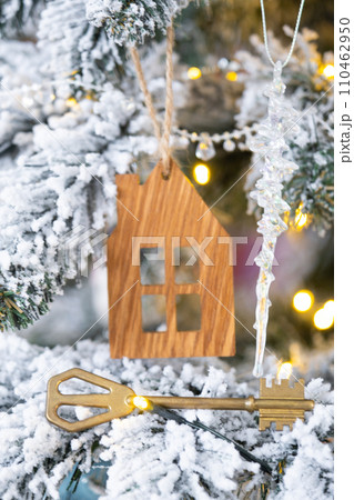 Key and tiny house keychain in hand on background fairy lights Christmas tree. gift for New Year, Christmas. Building, design, project, moving, insurance, mortgage, rent and purchase real estate. Key and tiny house keychain in hand on background fairy lights Christmas tree. gift for New Year, Christmas. Building, design, project, moving, insurance, mortgage, rent and purchase real estate. 110462950