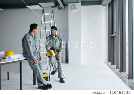 Builders in grey uniform talking after finishing work in building after construction Builders in grey uniform talking after finishing work in building after construction 110463530