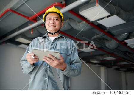 Portrait of smiling builder with digital tablet inspecting construction site and filling form on tablet computer 110463553
