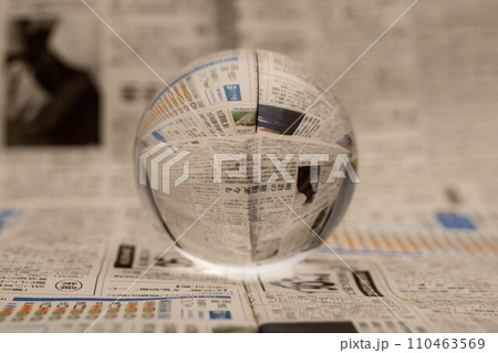 A glass globe reveals the letters inside, with a newspaper in the background. 110463569