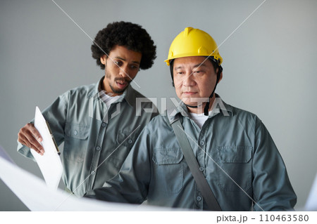 Diverse team of construction workers discussing details of building blueprint 110463580