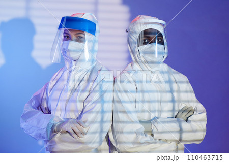 Medium shot of diverse man and woman laboratory technicians in white hazmat suits and face shields standing shoulder to shoulder while looking at camera Medium shot of diverse man and woman laboratory technicians in white hazmat suits and face shields standing shoulder to shoulder while looking at camera 110463715