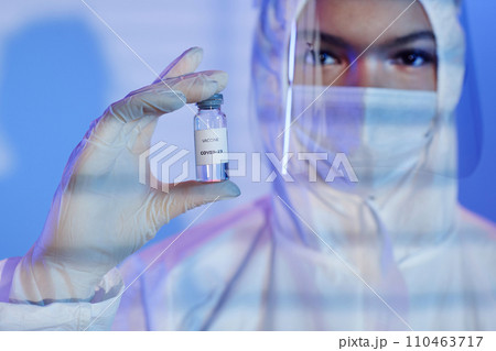 Close up shot of glass medical ampoule vial with COVID-19 vaccine in gloved hand of unrecognizable laboratory scientist dressed in hazmat suit Close up shot of glass medical ampoule vial with COVID-19 vaccine in gloved hand of unrecognizable laboratory scientist dressed in hazmat suit 110463717