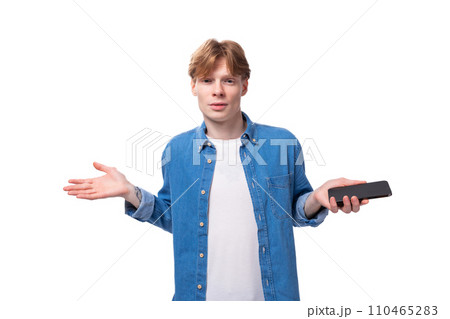 a young red-haired guy dressed in a blue shirt over a T-shirt spreads his arms in surprise a young red-haired guy dressed in a blue shirt over a T-shirt spreads his arms in surprise 110465283
