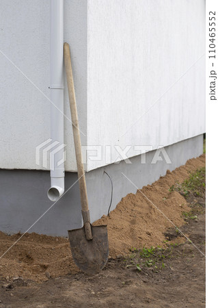 Preparation for laying tiles around a block house. A shovel and the wall of a white house. Preparation for laying tiles around a block house. A shovel and the wall of a white house. 110465552