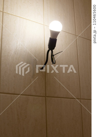 An energy-saving light bulb in a socket with a black wire on a beige wall. The concept of caring for nature. 110465600