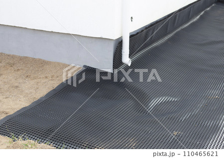 Laying a black waterproofing membrane around the foundation of a house. Construction of the blind area of the house. Reliable protection of the foundation from moisture. White pipe for draining 110465621