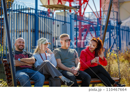 Group of friends enjoying conversations while swinging on a swing Group of friends enjoying conversations while swinging on a swing 110467664