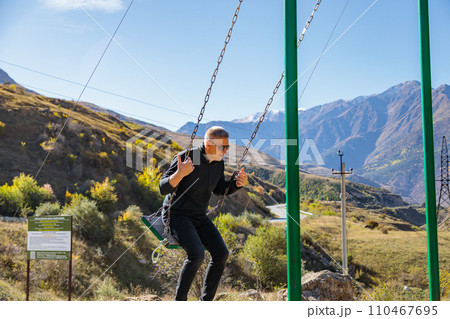 Man relaxing on a swing while enjoying the surrounding mountains and vast landscape 110467695