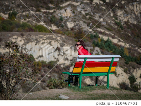 Girl on the background of mountains sitting on a bench Girl on the background of mountains sitting on a bench 110467701