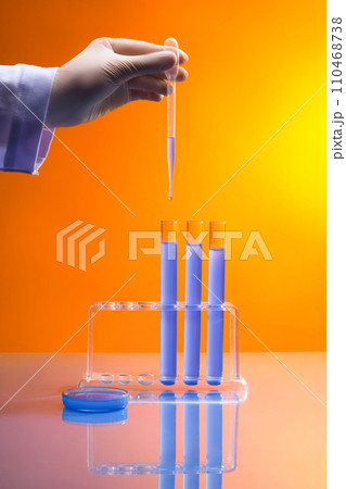 Professional scientist is dripping some liquid from a pipette to few test tubes displayed on a rack. A petri dish with blue chemical featured. Testing modern technological tools Professional scientist is dripping some liquid from a pipette to few test tubes displayed on a rack. A petri dish with blue chemical featured. Testing modern technological tools 110468738