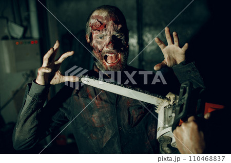 Walking zombie dead man and chainsaw attack on horror halloween party. 110468837