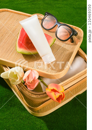 Picnic basket containing folded towel and some tulip flowers inside. A sunglasses, a slice of watermelon and unbranded tube displayed. The concept of summer vacation, skin and face care Picnic basket containing folded towel and some tulip flowers inside. A sunglasses, a slice of watermelon and unbranded tube displayed. The concept of summer vacation, skin and face care 110469350
