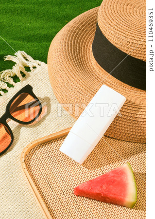 On a scarf, unlabeled white tube decorated with a beach hat, watermelon slice and a sunglasses. Concept of recovery, sun protection and moisturizing product On a scarf, unlabeled white tube decorated with a beach hat, watermelon slice and a sunglasses. Concept of recovery, sun protection and moisturizing product 110469351